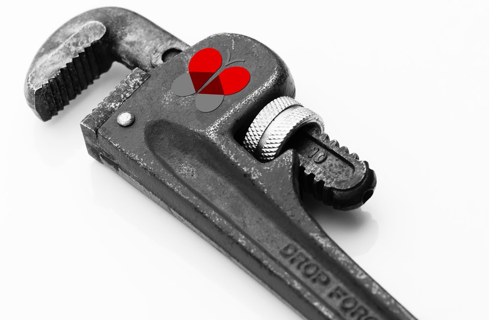 A heavy drop-forged pipe wrench photographed against white in high-contrast black and white, with the red Visova butterfly mark sited on the flat of the jaw as the only color in the frame.